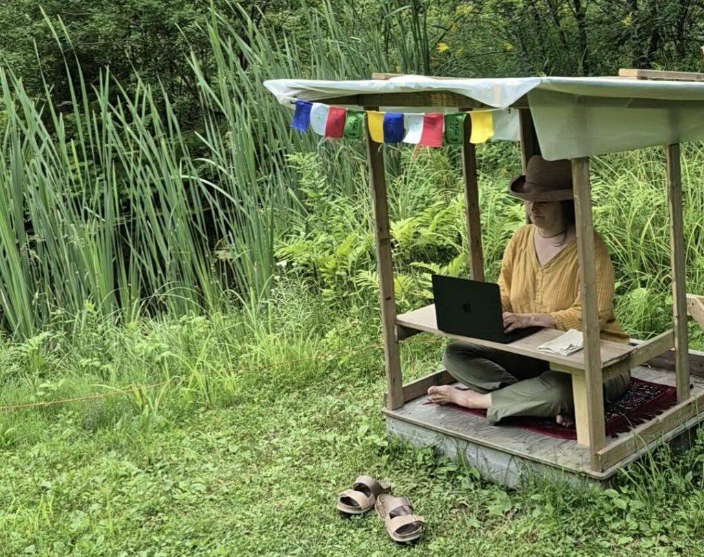 Carolyn Anne sitting in her garden micro-office the size of a meditation box